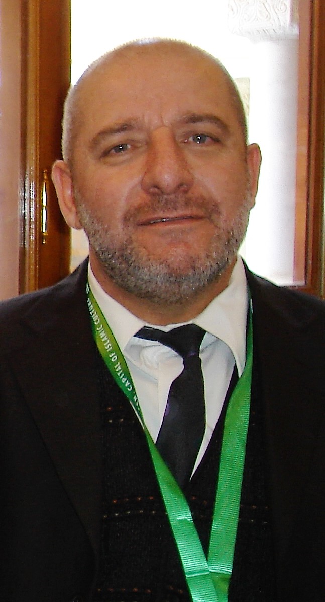 A portrait of a person wearing a jacket, tie and green lanyard.